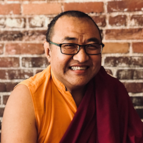 Tromge Jigme Rinpoche smiling, in robes, by a wall